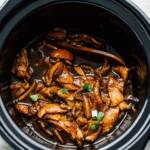 Crock Pot Bourbon Chicken served over rice with a glossy, caramelized sauce and garnished with green onions.