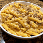 A skillet of creamy Garlic Butter Three Cheese Beef Penne topped with melted cheddar, mozzarella, and Parmesan, with tender penne pasta coated in rich sauce.