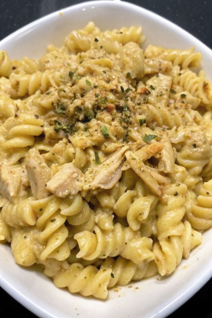 Close-up of Slow Cooker Garlic Parmesan Chicken Pasta topped with Parmesan cheese and garnished with herbs.