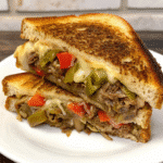 Philly Steakhouse Grilled Cheese sandwich with melted provolone, sautéed peppers, onions, and thinly shaved ribeye on toasted bread.