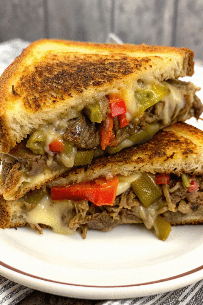 Close-up of a Philly Steakhouse Grilled Cheese sandwich cut in half, showing melted cheese and steak filling.