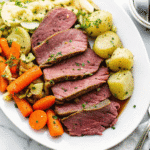 Tender sliced corned beef with cabbage, carrots, and baby potatoes served on a white plate.