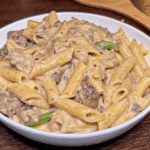 A skillet of creamy steak and cheese pasta with tender ribeye, sautéed onions, bell peppers, and melted mozzarella coating perfectly cooked penne pasta.