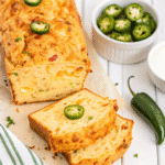 Freshly baked Jalapeño Cheddar Bread loaf sliced on a wooden board with visible melted cheddar and diced jalapeños.
