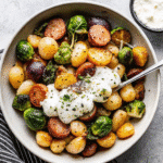 Golden roasted gnocchi with Brussels sprouts, squash, and Italian sausage on a sheet pan, topped with creamy burrata and a drizzle of pesto.