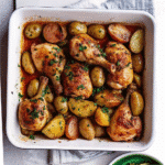 Golden roasted One Pan Chicken and Potatoes with crispy skin, tender baby potatoes, garlic, and lemon in a baking dish.