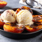 Grilled peach halves topped with melted butter and brown sugar, served with a scoop of vanilla ice cream on a white plate.
