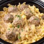 Crockpot Swedish Meatballs in creamy mushroom sauce with egg noodles, garnished with parsley, served in a white bowl.