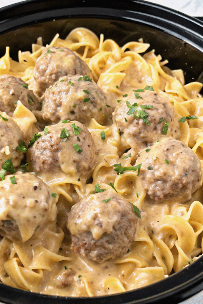 Close-up of Crockpot Swedish Meatballs simmering in a rich, creamy sauce with chopped onions and parsley on top.