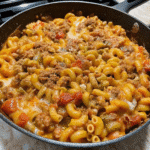 Cheesy Sloppy Joe Pasta in a skillet with ground beef, elbow pasta, tomato sauce, and melted cheddar cheese