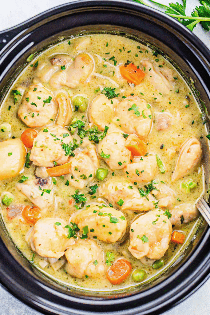 Slow-cooked chicken and dumplings in a crockpot with golden biscuits and fresh parsley garnish