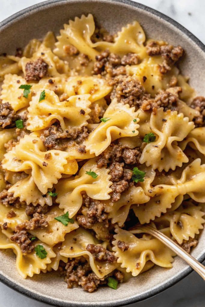 Close-up of bowtie pasta coated in garlic butter with browned ground beef and herbs