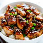 Easy Chicken Teriyaki served in a bowl with glossy teriyaki sauce, sesame seeds, and rice on the side.