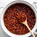 Homemade baked beans in a skillet topped with crispy bacon, baked until thick, bubbly, and caramelized