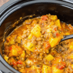 Crockpot Cheesy Taco Potatoes topped with melted cheddar, seasoned ground beef, and tender diced potatoes in a serving bowl.