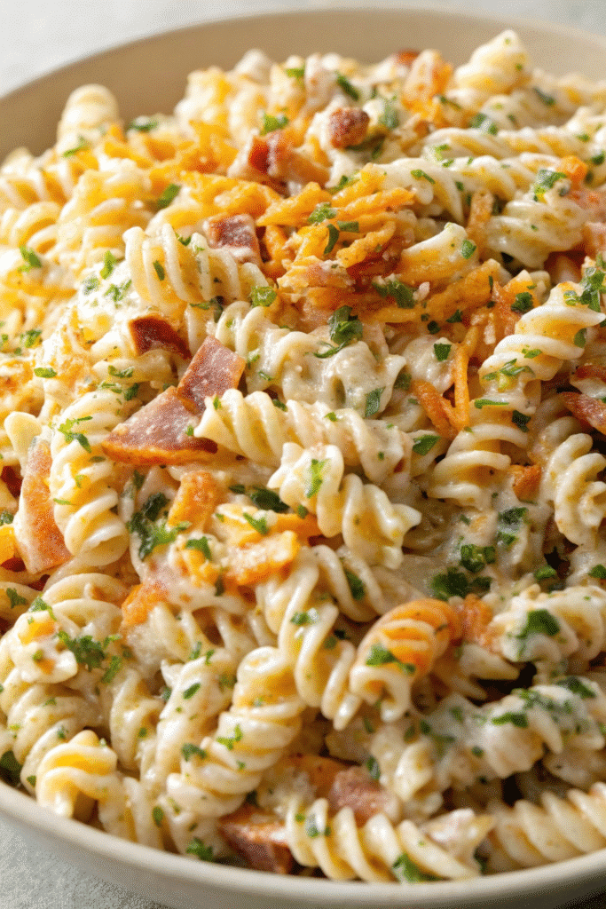 Close-up of Chicken Bacon Ranch Pasta Salad with rotini, bacon crumbles, chicken pieces, cucumber, tomatoes, and creamy ranch coating.