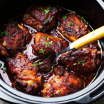 CrockPot Chicken Thighs served in a bowl with glossy honey garlic sauce and fresh parsley on top.