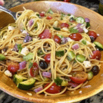 Bowl of California Spaghetti Salad with spaghetti, cucumbers, cherry tomatoes, olives, and mozzarella tossed in Italian dressing.