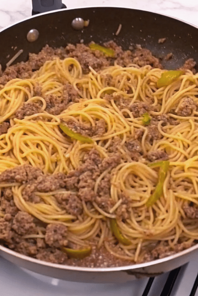Close-up of Cheesy Beef Angel Hair Spaghetti coated in a rich beef sauce with visible herbs and peppers