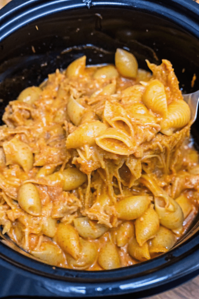 Slow cooker BBQ chicken mac and cheese served warm, showing cheesy pasta shells mixed with shredded chicken in a creamy barbecue sauce.