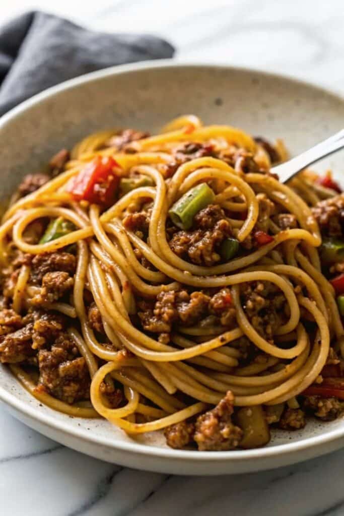 Close-up of Dirty Spaghetti mixed with seasoned meat, garlic, and glossy gravy-style sauce