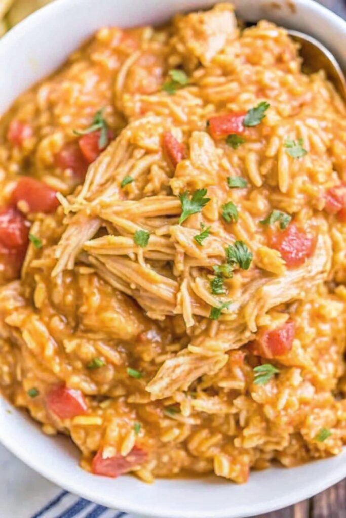 Slow-cooked taco chicken mixed with cheesy rice and tomatoes in a rustic bowl, garnished with avocado and shredded cheese.