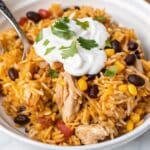 Chicken Burrito Bowl Bake topped with melted cheddar cheese, sour cream, and fresh cilantro in a baking dish.